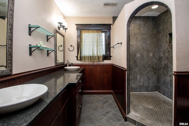 bathroom with a sink, visible vents, a tile shower, and wainscoting