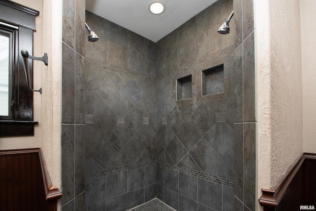 full bath featuring a tile shower and a textured wall