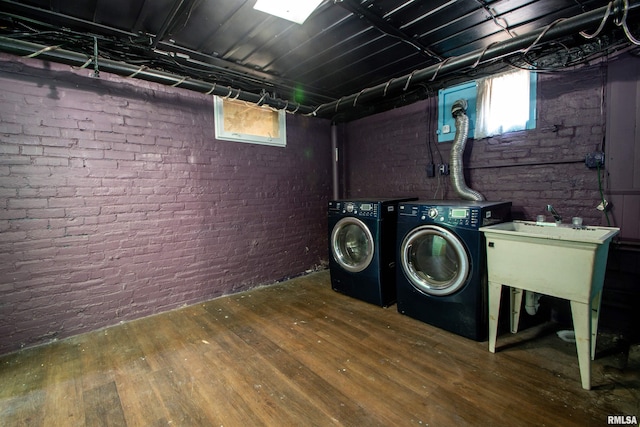 clothes washing area featuring hardwood / wood-style floors, washing machine and clothes dryer, laundry area, and brick wall