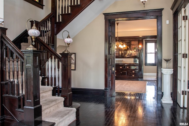 foyer entrance with hardwood / wood-style floors, baseboards, a notable chandelier, and stairway