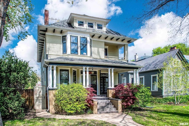 american foursquare style home featuring fence, covered porch, and a chimney