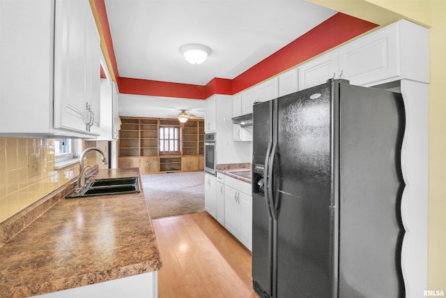 kitchen with under cabinet range hood, black appliances, backsplash, a sink, and white cabinetry