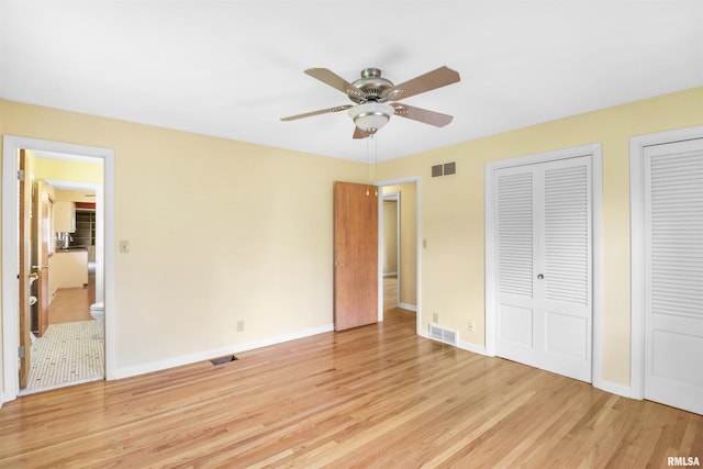 unfurnished bedroom with visible vents, ensuite bathroom, baseboards, light wood-type flooring, and two closets
