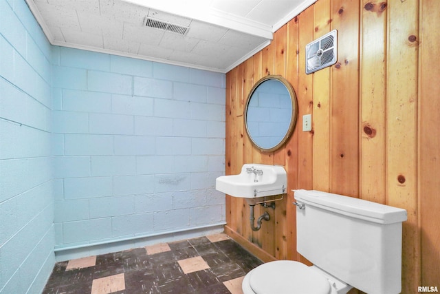 half bath with a sink, tile patterned floors, toilet, visible vents, and wood walls