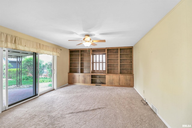 unfurnished living room with carpet floors, built in shelves, baseboards, visible vents, and a ceiling fan