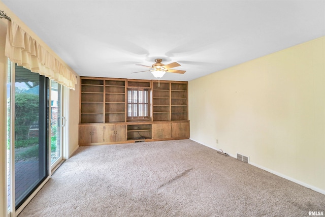 carpeted spare room with baseboards, visible vents, built in shelves, and ceiling fan