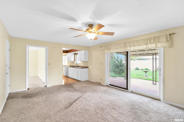 unfurnished living room with baseboards, light carpet, ceiling fan, and a sink