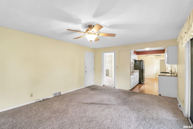 unfurnished living room with a sink, visible vents, baseboards, light carpet, and a ceiling fan