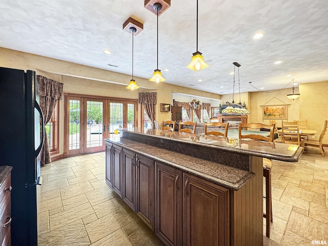 kitchen with freestanding refrigerator, french doors, a breakfast bar area, and stone tile floors