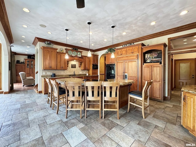 kitchen with brown cabinets, a breakfast bar area, arched walkways, a large island, and tasteful backsplash