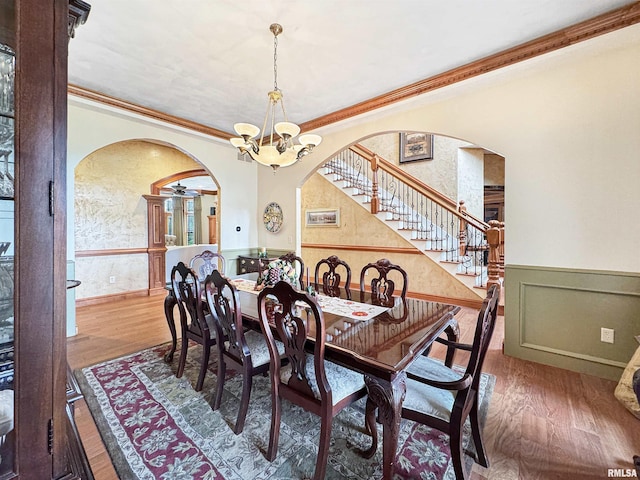 dining room with stairway, arched walkways, wainscoting, and wood finished floors