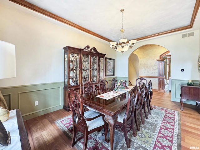 dining room with visible vents, wood finished floors, a wainscoted wall, arched walkways, and a notable chandelier