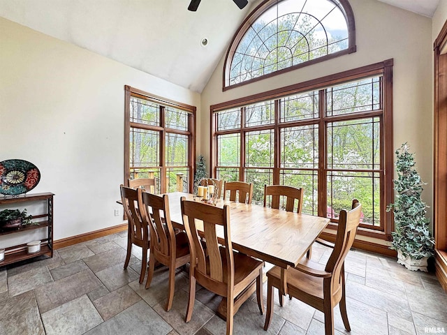 dining area featuring baseboards, stone tile floors, ceiling fan, and high vaulted ceiling