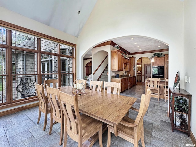 dining space featuring crown molding, arched walkways, high vaulted ceiling, stone tile floors, and recessed lighting