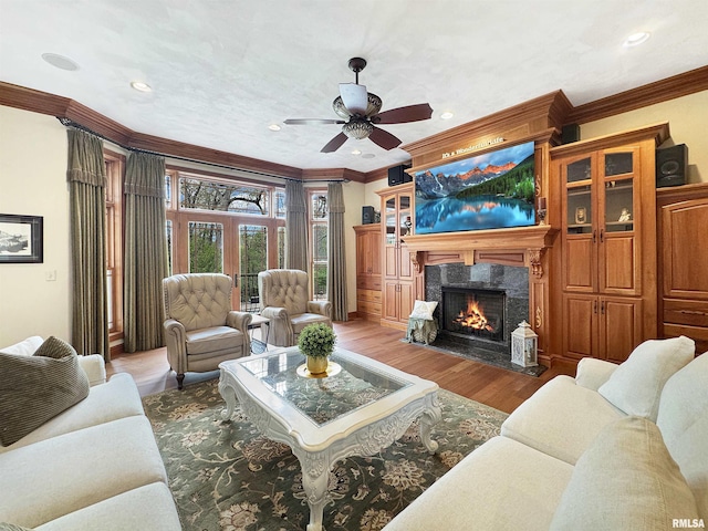 living area with ornamental molding, a fireplace, a ceiling fan, and wood finished floors