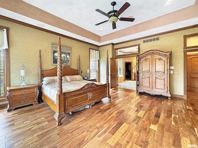 bedroom featuring visible vents, multiple windows, a raised ceiling, and light wood-type flooring