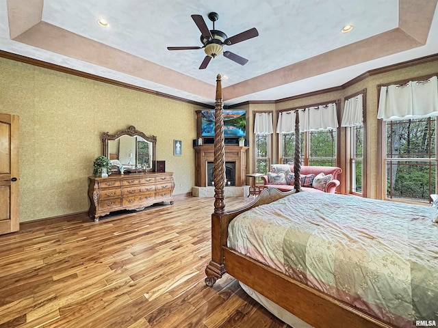 bedroom with a fireplace with raised hearth, a tray ceiling, ornamental molding, and hardwood / wood-style flooring