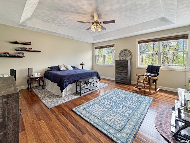 bedroom with baseboards, a ceiling fan, a raised ceiling, and wood finished floors