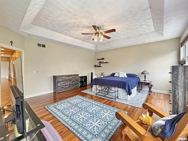 bedroom with a tray ceiling, visible vents, baseboards, and wood finished floors