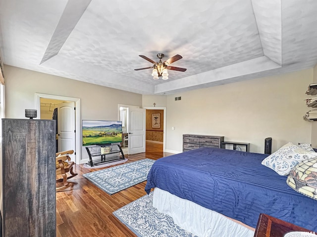 bedroom with ceiling fan, visible vents, wood finished floors, baseboards, and a tray ceiling