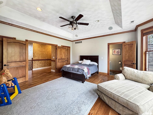 bedroom with baseboards, wood finished floors, a tray ceiling, and visible vents