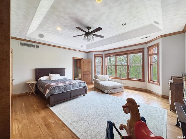 bedroom with baseboards, a tray ceiling, light wood-type flooring, and visible vents