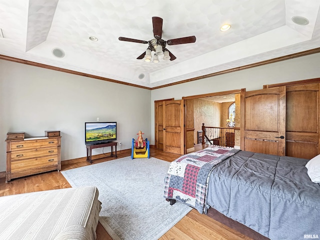 bedroom featuring ceiling fan, crown molding, light wood-type flooring, baseboards, and a tray ceiling