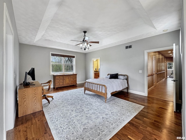 bedroom with visible vents, baseboards, ceiling fan, dark wood-type flooring, and a raised ceiling