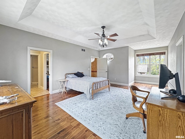 bedroom with baseboards, a raised ceiling, and wood finished floors