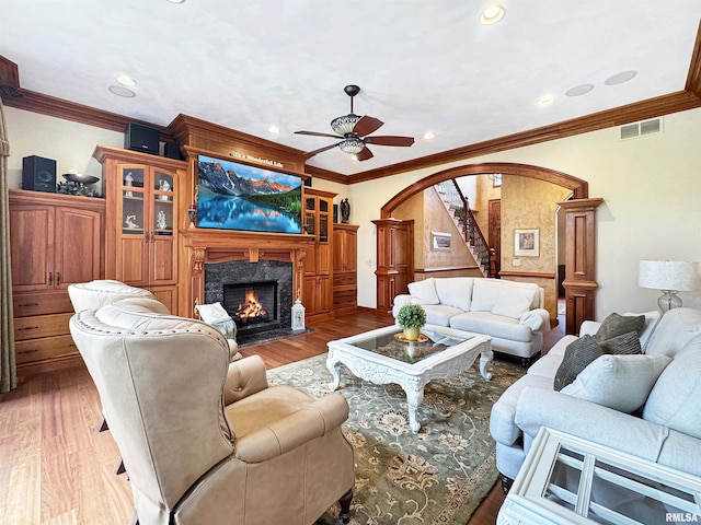 living area with a ceiling fan, visible vents, arched walkways, a fireplace, and ornamental molding