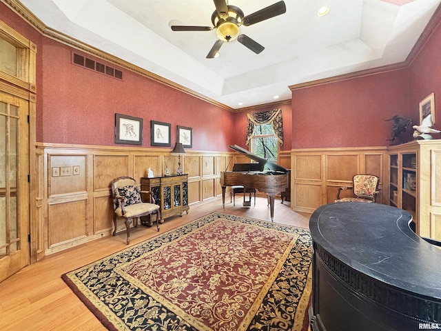 living area with a raised ceiling, a wainscoted wall, light wood finished floors, and visible vents