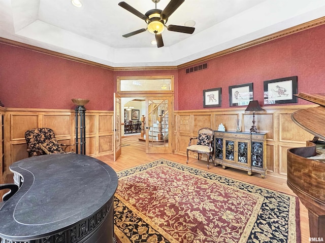 living area featuring visible vents, wood finished floors, a decorative wall, ceiling fan, and a raised ceiling