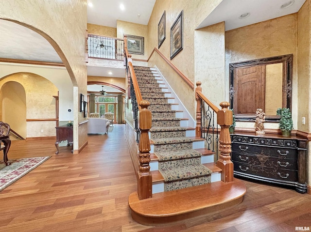 entryway with arched walkways, a high ceiling, ceiling fan, and wood finished floors