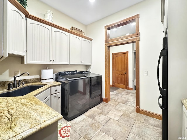 clothes washing area with baseboards, a sink, cabinet space, and washing machine and clothes dryer