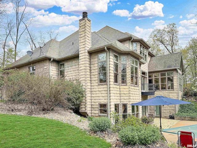 exterior space featuring a yard, a patio, a chimney, and a shingled roof