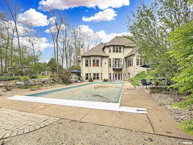 back of property with a shingled roof, a chimney, a covered pool, and a patio area