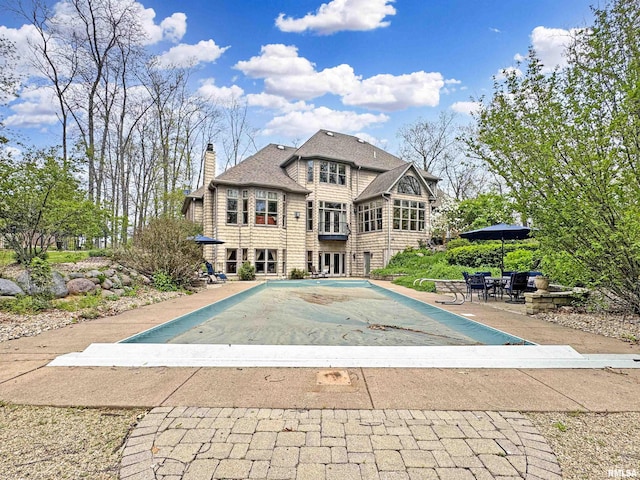 rear view of house with roof with shingles, a chimney, a covered pool, and a patio area
