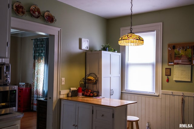 kitchen featuring stainless steel microwave, hanging light fixtures, wainscoting, and a wealth of natural light