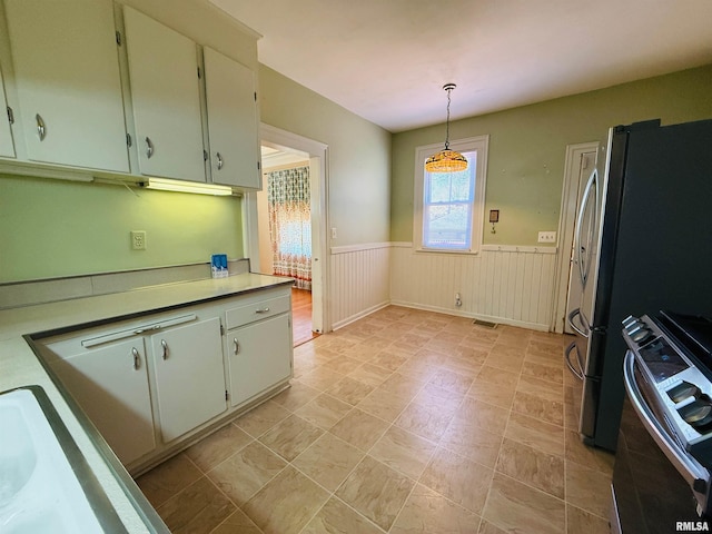 kitchen with stainless steel range oven, a wainscoted wall, hanging light fixtures, and light countertops