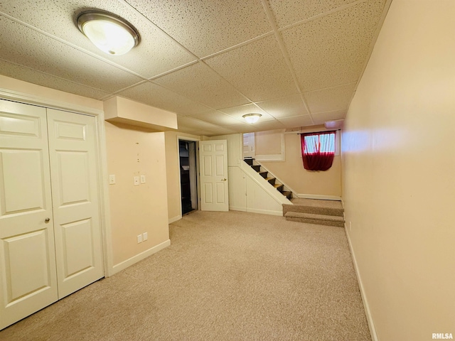 below grade area featuring baseboards, light carpet, stairs, and a drop ceiling