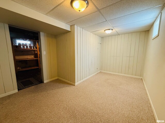 finished below grade area with baseboards, wooden walls, carpet flooring, and a paneled ceiling