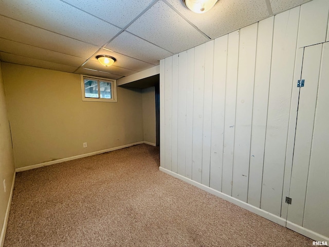 below grade area featuring baseboards, wooden walls, carpet, and a paneled ceiling