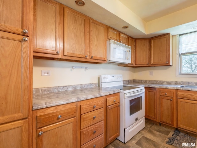 kitchen featuring brown cabinetry, white appliances, light countertops, and a sink