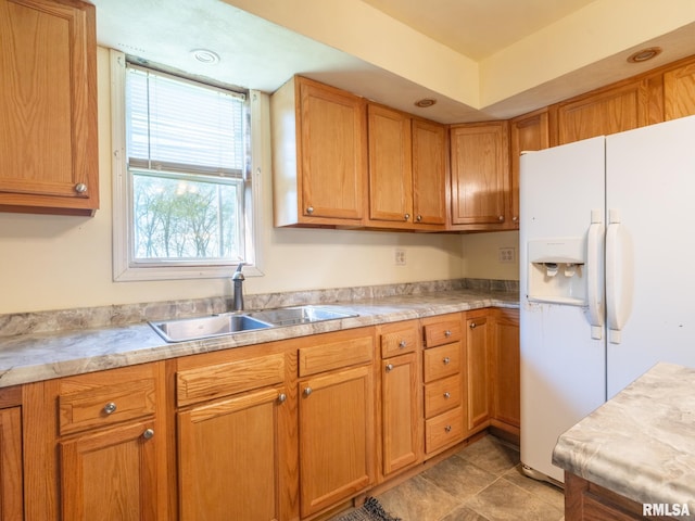 kitchen with brown cabinetry, light countertops, white refrigerator with ice dispenser, and a sink