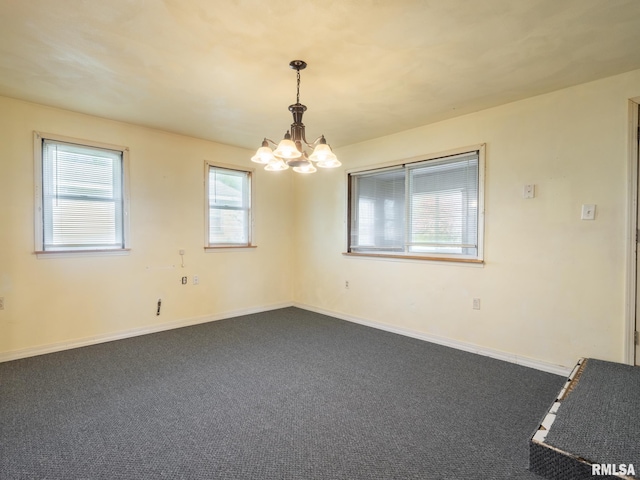 empty room with dark colored carpet, a chandelier, and baseboards