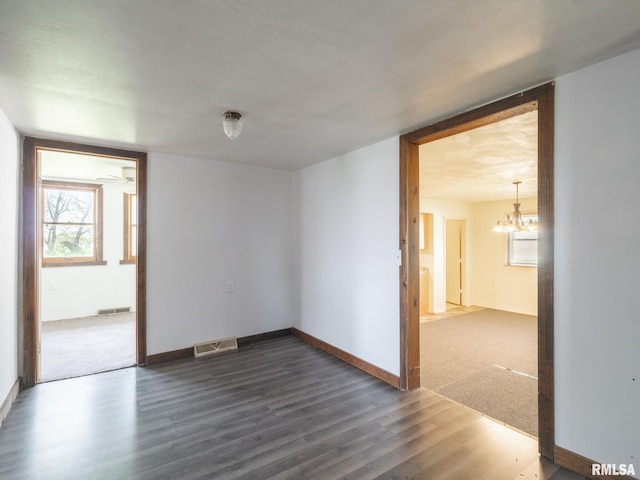 unfurnished room with dark wood-style floors, visible vents, a chandelier, and baseboards