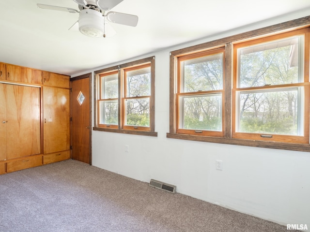 carpeted empty room featuring a ceiling fan, visible vents, and plenty of natural light