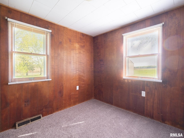 carpeted empty room featuring visible vents, wood walls, and plenty of natural light