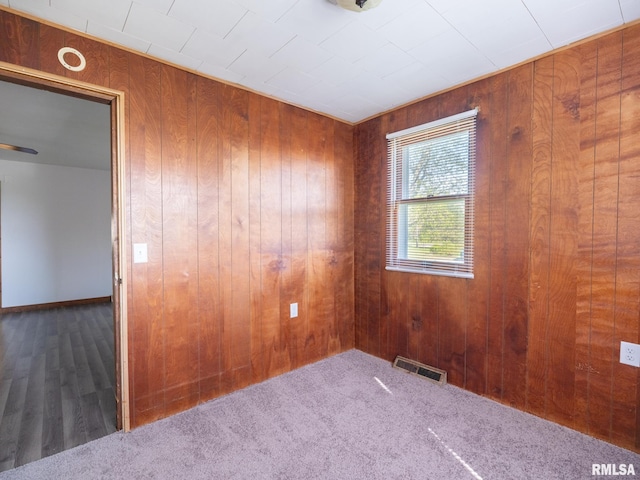 carpeted spare room with visible vents and wood walls