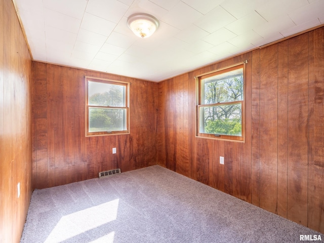 carpeted empty room featuring visible vents and wood walls